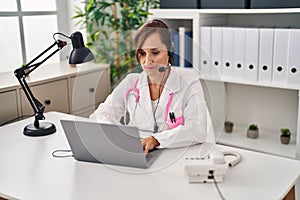 Middle age doctor woman working wearing headset thinking attitude and sober expression looking self confident