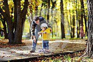 Middle age father showing his toddler son how to ride a scooter in a autumn park