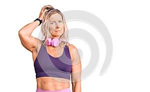 Middle age fit blonde woman wearing gym clothes and using headphones confuse and wonder about question