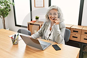 Middle age grey-haired call center agent woman smiling happy working at the office