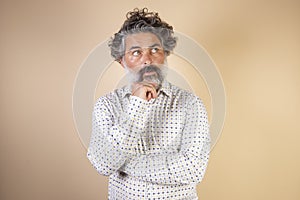 Middle age grey-haired man in casual clothes with hand on chin thinking about question, expression of penitence. doubt concept photo