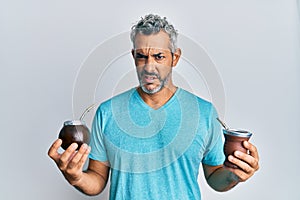 Middle age grey-haired man drinking mate infusion clueless and confused expression
