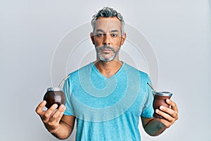 Middle age grey-haired man drinking mate infusion relaxed with serious expression on face