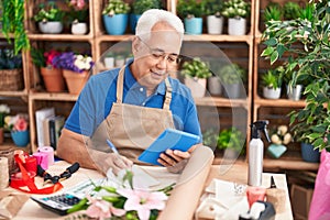 Middle age grey-haired man florist using touchpad writing on notebook at florist