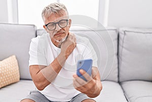 Middle age grey-haired man having teleconsultation sitting on sofa at home photo
