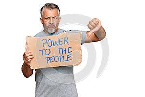 Middle age grey-haired man holding power to the people banner with angry face, negative sign showing dislike with thumbs down,