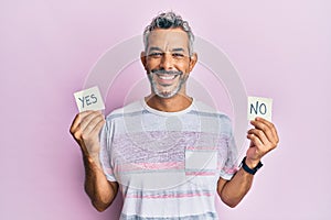 Middle age grey-haired man holding yes and no reminder smiling with a happy and cool smile on face