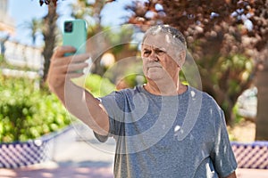 Middle age grey-haired man make selfie by smartphone with relaxed expression at park