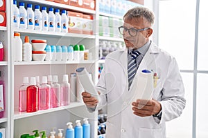 Middle age grey-haired man pharmacist holding shampoo bottles at laboratory