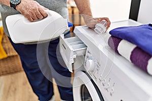 Middle age grey-haired man pouring detergent on washing machine at home