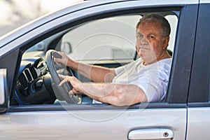 Middle age grey-haired man smiling confident driving car at street
