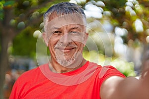 Middle age grey-haired man smiling confident making selfie by camera at park