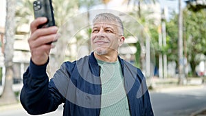 Middle age grey-haired man smiling confident making selfie by the smartphone at park