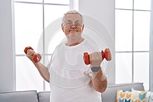 Middle age grey-haired man smiling confident using dumbbells training at home