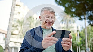 Middle age grey-haired man smiling confident watching video on smartphone at park