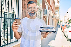 Middle age grey-haired man smiling happy holding cup of coffee and take away food at the city