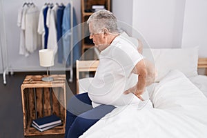 Middle age grey-haired man suffering for back injury sitting on bed at bedroom