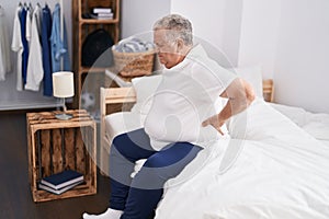 Middle age grey-haired man suffering for back injury sitting on bed at bedroom