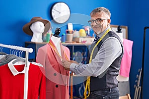 Middle age grey-haired man tailor smiling confident measuring jacket at clothing factory