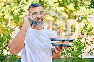 Middle age grey-haired man talking on the smartphone and holding take away food at the park