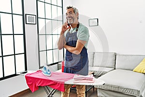 Middle age grey-haired man talking on smartphone ironing clothes at home