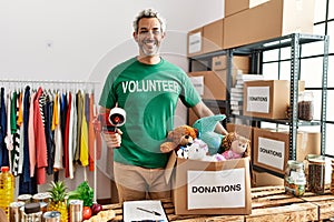 Middle age grey-haired man volunteer smiling confident holding packing machine at charity center