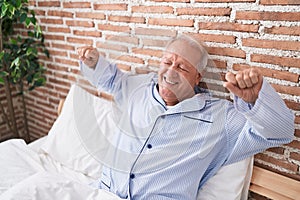 Middle age grey-haired man waking up stretching arms at bedroom