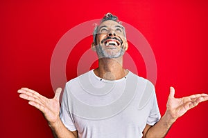 Middle age grey-haired man wearing casual white tshirt celebrating mad and crazy for success with arms raised and closed eyes