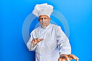 Middle age grey-haired man wearing professional cook uniform and hat disgusted expression, displeased and fearful doing disgust