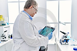 Middle age grey-haired man wearing scientist uniform looking embryology image touchpad at laboratory