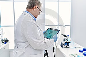 Middle age grey-haired man wearing scientist uniform looking embryology image touchpad at laboratory