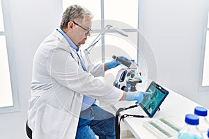 Middle age grey-haired man wearing scientist uniform looking embryology image touchpad at laboratory