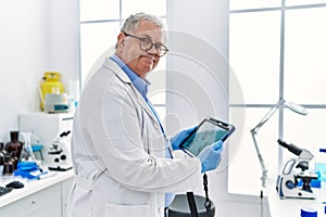 Middle age grey-haired man wearing scientist uniform looking embryology image touchpad at laboratory