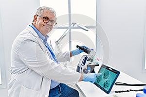 Middle age grey-haired man wearing scientist uniform looking embryology image touchpad at laboratory