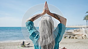 Middle age grey-haired woman doing yoga exercise at beach