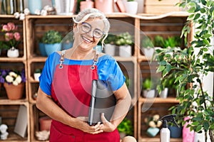 Middle age grey-haired woman florist smiling confident holding binder at florist