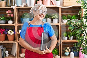 Middle age grey-haired woman florist smiling confident holding binder at florist