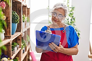 Middle age grey-haired woman florist smiling confident writing on document at florist