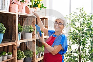 Middle age grey-haired woman florist using touchpad holding plant at florist