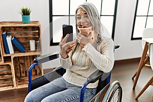 Middle age grey-haired woman having teleconsultation sitting on wheelchair at home