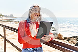 Middle age grey-haired woman having video call using touchpad at the beach