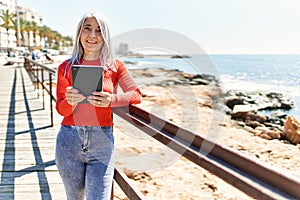 Middle age grey-haired woman smiling happy using touchpad at the beach