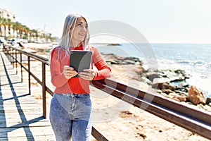 Middle age grey-haired woman smiling happy using touchpad at the beach