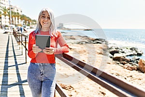 Middle age grey-haired woman smiling happy using touchpad at the beach