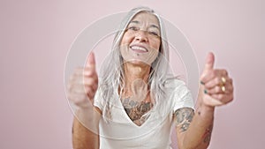 Middle age grey-haired woman smiling with thumbs up over isolated pink background