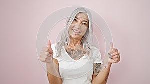 Middle age grey-haired woman smiling with thumbs up over isolated pink background