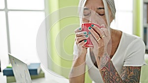 Middle age grey-haired woman student using laptop smelling coffee at library university