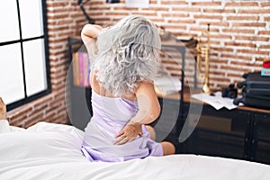 Middle age grey-haired woman suffering for back injury sitting on bed at bedroom