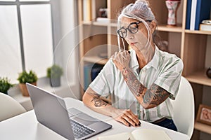 Middle age grey-haired woman suffering for shoulder pain using laptop at home