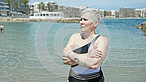 Middle age grey-haired woman tourist wearing swimsuit standing with arms crossed gesture at the beach